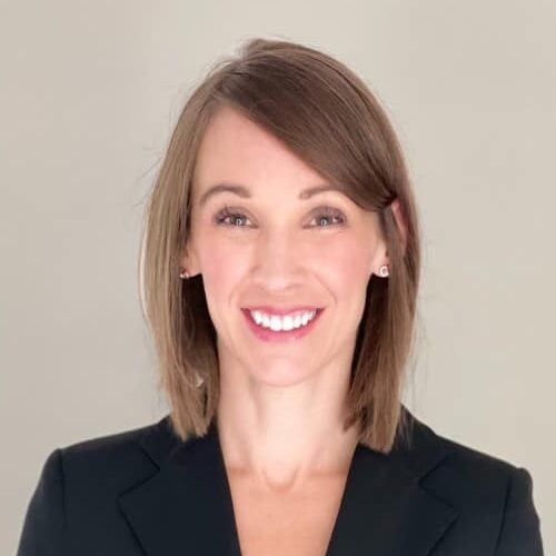 Professional headshot of a smiling woman with shoulder-length light brown hair, wearing a black blazer against a neutral background.