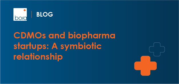 Blog banner: blue gradient background, orange headline 'CDMOs and biopharma startups: A symbiotic relationship' with an orange plus icon on the right.